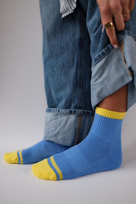 Person wearing blue jeans and blue socks with yellow accents on a white background